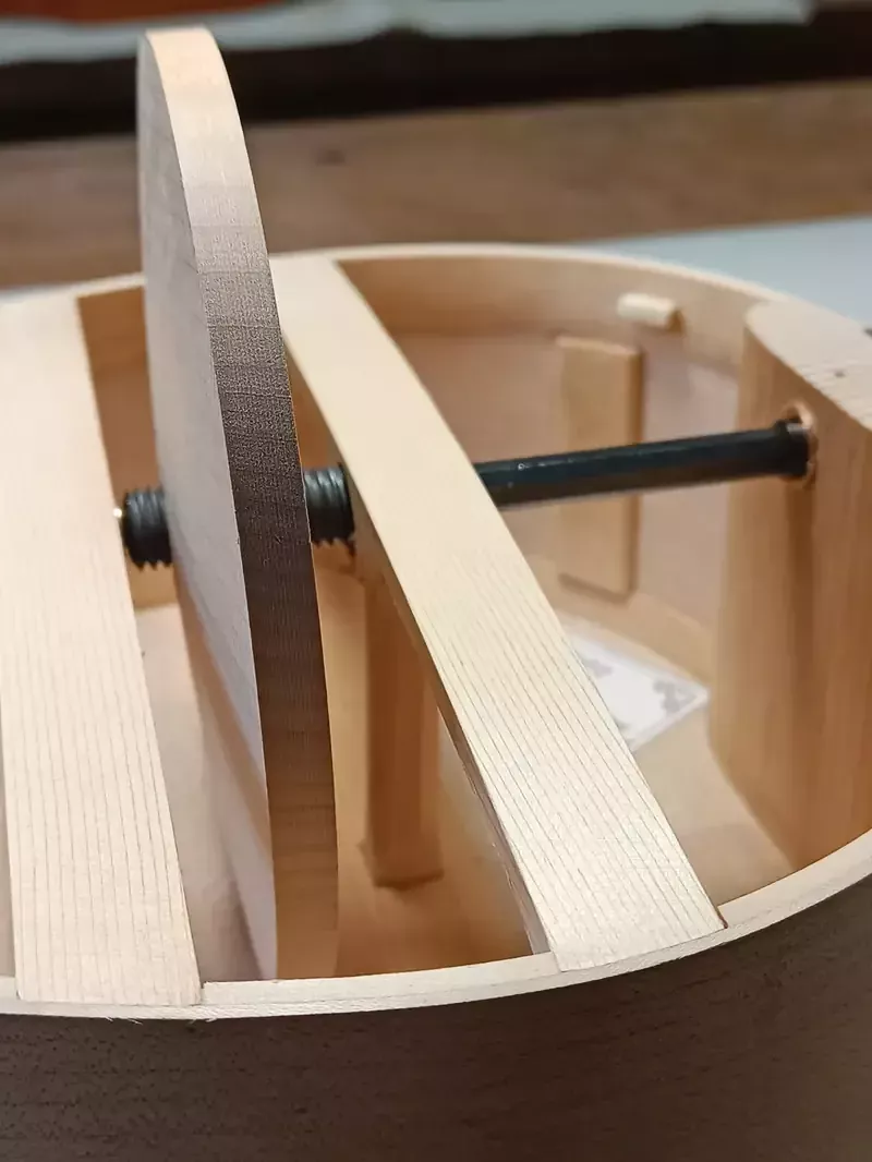 Detail van de binnenkant van een draailier. Je ziet een rond, houten wiel. Door het midden van het wiel loopt een metalen staaf.