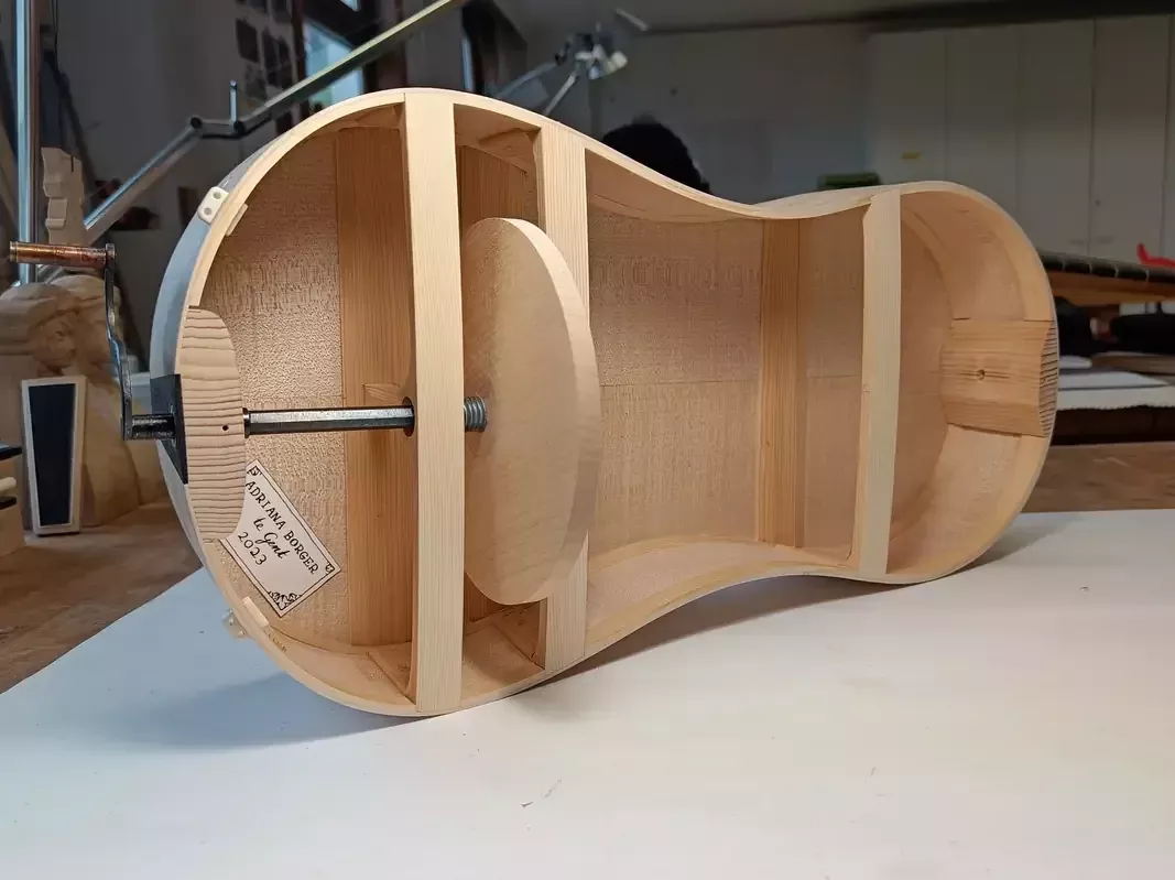 Binnenkant van een gitaarvormige draailier. Links zie je een houten wiel, met daardoor een metalen staafje (lager) dat verbonden is met de metalen zwengel.